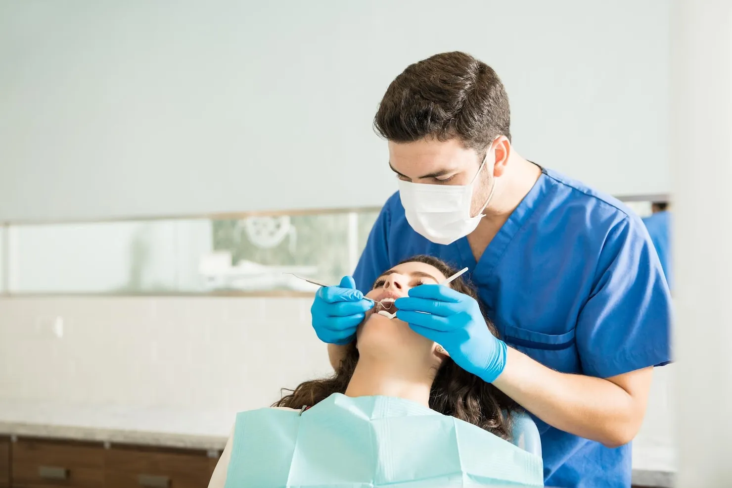 Male dentist examining young woman before wisdom teeth removal procedure