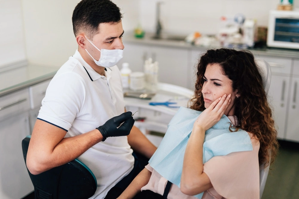 A female patient holding her jaw in pain during a dental consultation for a suspected dry socket complication.