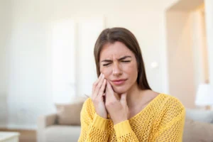 A woman holding her jaw in severe discomfort, illustrating typical dry socket pain symptoms after a tooth extraction.