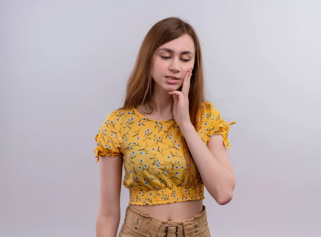 A young woman holding her hand to her sore cheek, illustrating common wisdom teeth pain symptoms.